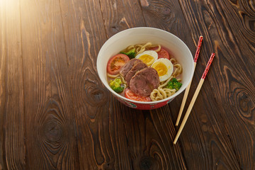 Asian noodle soup with vegetables, egg, beef and chopsticks on wooden background and copy space