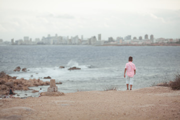 A child walks on the sea coast, he is wearing a coral shirt, the boy travels along the sea, outdoor