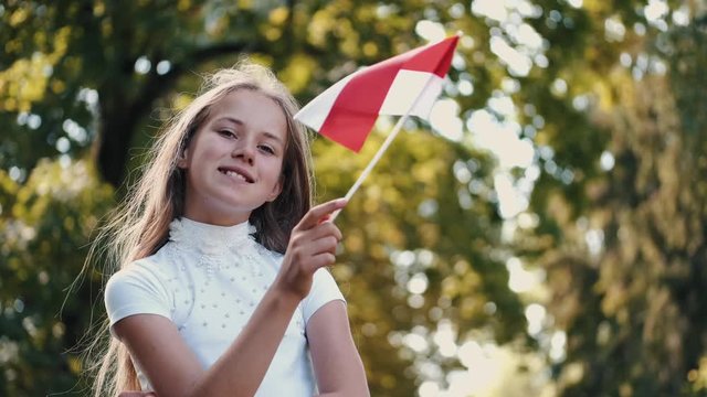 Girl holds Polish flag. Green background is blurred. Kid is in park holding stick.