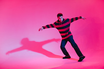 Fototapeta na wymiar Young Man in a Jumper Dancing Contemporary Dance in Studio. Breakdancing. Dance School Poster. Copy Space. Battle competition announcement. Pink and Blue Background.