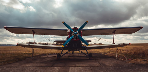 Front view to biplane standing on airports with cloud sky - obrazy, fototapety, plakaty