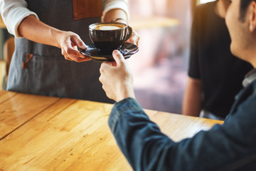 A waitress holding and serving a cup of hot coffee to a male customer in cafe