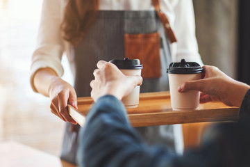 A waitress holding and serving paper cups of hot coffee to customer in cafe