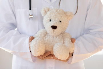Close up young pediatrician in white coat holding toy in hands, showing professional friendly attitude to children. General practitioner demonstrating stress free doctor visit, healthcare concept.