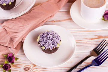 Chocolate delicious cupcake with cream and fragrant coffee with milk on a white wooden table.