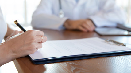 Close up young woman holding pen, ready to sign medical insurance contract with family doctor....