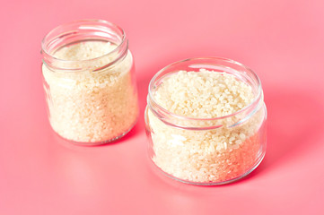 Two jars of grain of rice on pink background