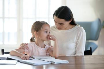 Unhappy little school girl stuck with hard task, feeling stressed. Worrying young mother embracing...