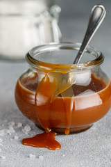 Homemade salted caramel in a glass jar. Delicious sauce with sea salt for ice cream and desserts. Selective focus