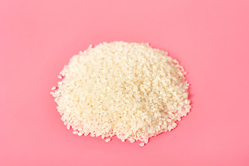 Heap of grain of white rice on pink background