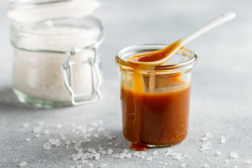 Homemade salted caramel in a glass jar. Delicious sauce with sea salt for ice cream and desserts. Selective focus