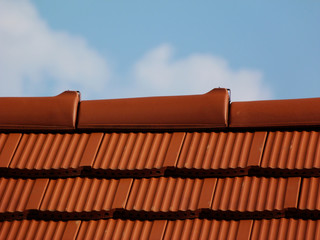 new sloped clay roof ridge closeup detail. bright red clay roofing. clear blue sky. light fluffy white clouds in bright sunlight. construction industry and residential building  materials.