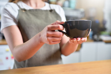 A young barista girl offers a large cup with coffee. Small business concept.