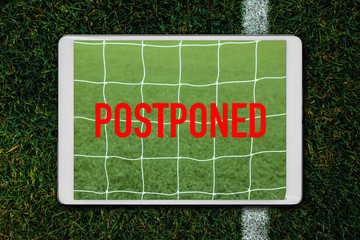 Digital tablet showing postponed soccer match on green grass soccer field background.