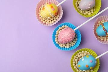 Egg shaped cake pops and space for text on violet background, flat lay. Easter celebration
