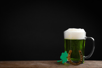 Green beer and clover on wooden table against black background, space for text. St. Patrick's Day celebration