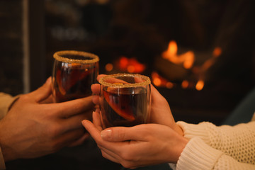 Couple with tasty mulled wine near fireplace indoors, closeup
