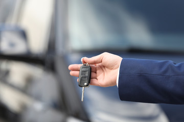 Man holding key in modern auto dealership, closeup. Buying new car