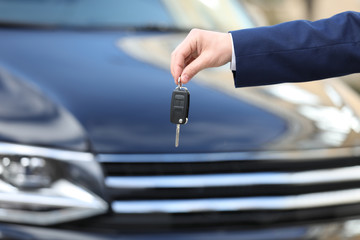Man holding key in modern auto dealership, closeup. Buying new car