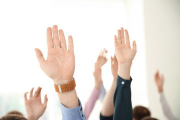 People raising hands to ask questions at business training on light background, closeup