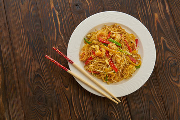 Asian delicious stir-fried noodles with shrimps, vegetables, red peppers and chopsticks on wooden background copy space