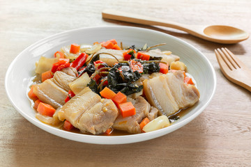 close up of stir fried pork belly with holy basil in a ceramic dish on wooden table. hot and spicy thai style food menu.