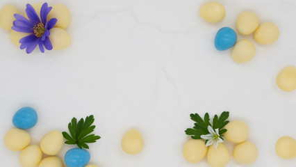 Blue and white flowers green leaves and candy Easter eggs on a scrunched plain white paper background with copy space