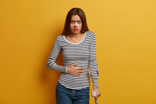 Indoor Shot Of Sick Woman Victim Of Reckless Driving Feels Discomfort In Stomach, Broken Nose And Leg, Uses Mobility Aid, Looks Sadly At Camera, Comes To See Surgeon, Recovers After Disaster