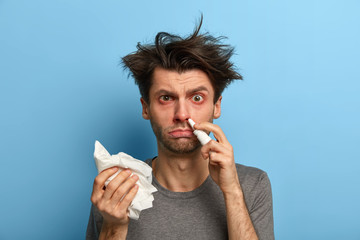 Home treatment, virus, seasonal illness and allergy concept. Dissatisfied man spays blocked nose,...