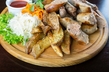 Homemade grilled sausages with sauerkraut and ketchup on a round wooden tray.