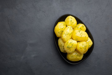 Delicious boiled potatoes with dill in a black plate on a dark background. Top view.