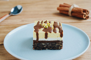 A piece of orange-chocolate cake. Spoon and cinnamon on a wooden background. Raw dessert with a nut base.