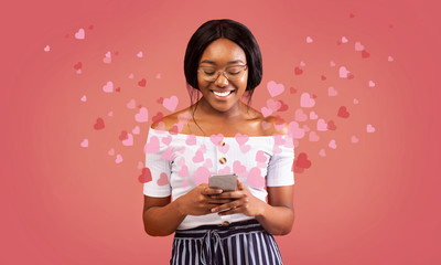 African American girl holding smartphone with hearts flying out of it on pick background, panorama