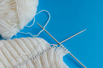 Knitting a scarf from wool yarn. Step by step. Learning to knit. Scarf made of white threads on a blue background.