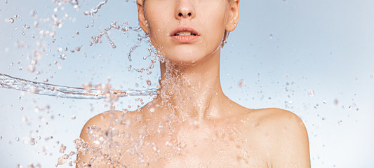 Stream of clear water splashes against a woman's body. Woman with drops of water around her face...