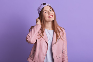 Image of pretty fair haired young female wearing pink leather jacket, white t shirt and lilac cap,...