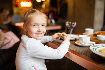 child sits at a table in a cafe. Happy little girl with blonde hair sitting in restaurant