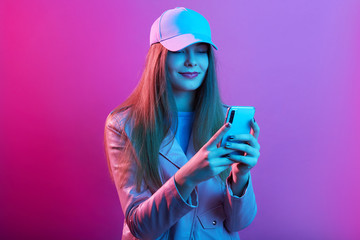 Stylish studio portrait of stylish girl wearing jacket and cap, woman holding phone in hands,...