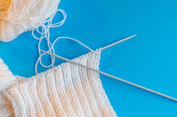 Knitting a scarf from wool yarn. Step by step. Learning to knit. Scarf made of white threads on a blue background.