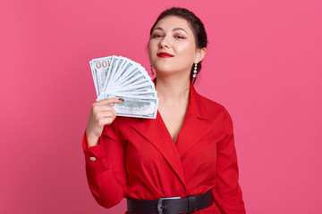 Image of successful confident pretty young brunette holding fan of cash money, having delighted...