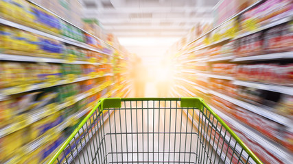 Supermarket aisle with empty green shopping cart.