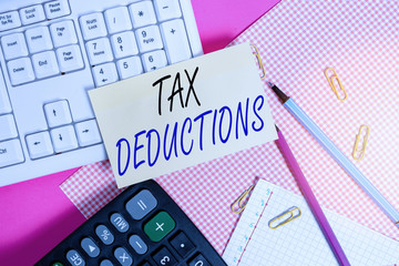 Handwriting text Tax Deductions. Conceptual photo reduction income that is able to be taxed of expenses Note paper stick to computer keyboard near colored gift wrap sheet on table