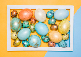 Colored Easter eggs in a wooden white frame on a colored background. Happy Easter!
