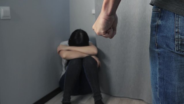 domestic violence concept clenched fist. husband beats wife. woman sits in a corner afraid is scared a man waves his fist at a woman at a family violence lifestyle