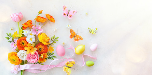 Holiday concept with bouquet of spring flowers, Easter eggs and butterfly on pastel vintage background. Easter composition