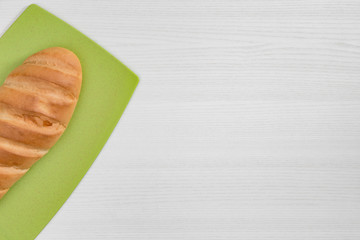 Whole loaf of bread on green board on white background.