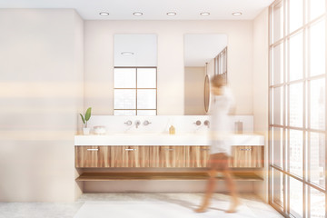 Woman walking in beige bathroom with double sink