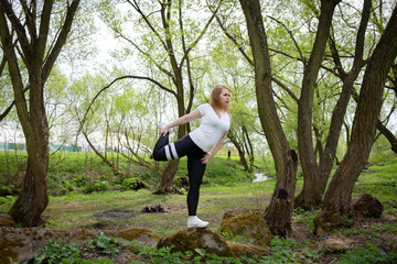 European young woman in a white top and black leggings doing fitness in nature