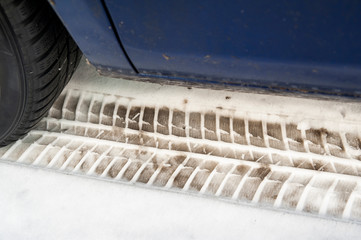 Close up of a car and winter tires. Very dirty car is parked on the street covered by snow.