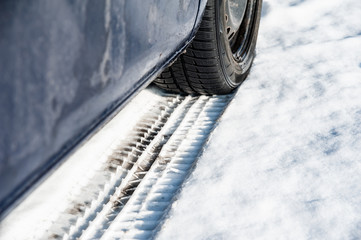 Close up of a car and winter tires. Very dirty car is parked on the street covered by snow.